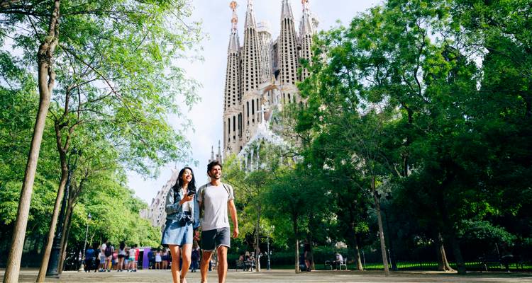 Jeune couple se promenant dans un parc verdoyant avec les flèches de la Sagrada Familia s'élevant à l'arrière-plan