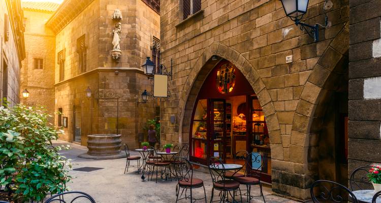 Ruelle de pierre charmante avec des tables de café en plein air et une porte voûtée éclairée par un chaud rayon de soleil à Barcelone.
