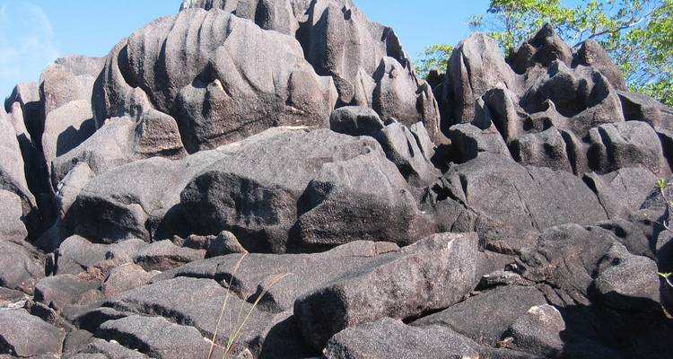 Jagged black granite formations rise against a blue sky and green foliage