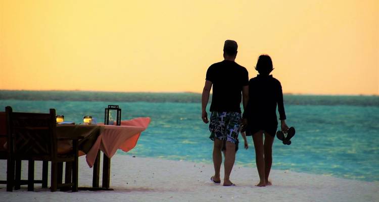 Couple strolls a candle-lit beach at dusk with a romantic dinner table nearby