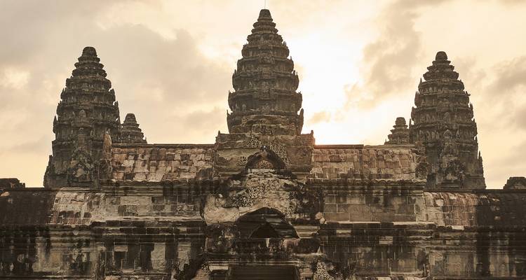 Vorderansicht von Angkor Wats fünf ikonischen Türmen, die sich gegen einen blassen Himmel bei Sonnenaufgang abzeichnen.