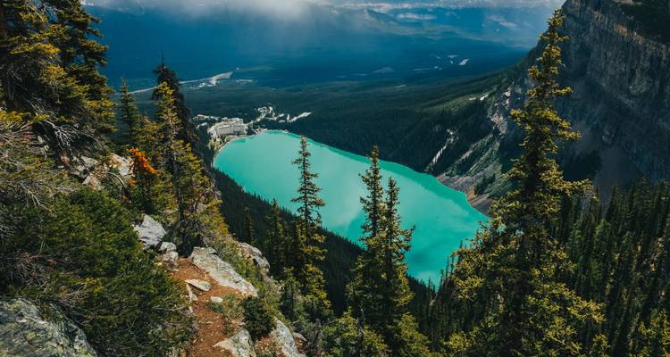 Point de vue élevé d'un lac turquoise éclatant sous de hautes montagnes forestières abruptes avec un lodge visible en bas.