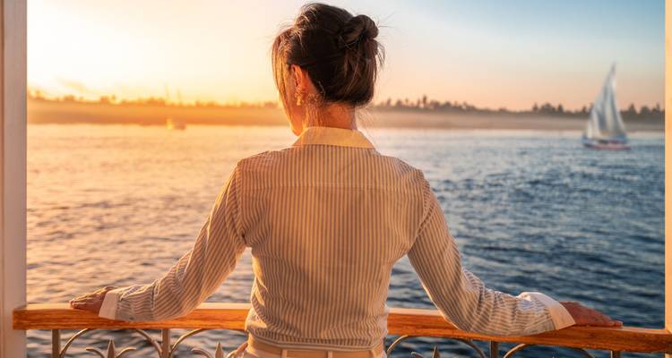 Back view of woman gazing over the Nile at sunset from a wooden deck railing