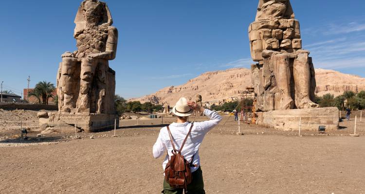 Traveler taking photo of the colossal statues of Memnon against desert mountains near Luxor