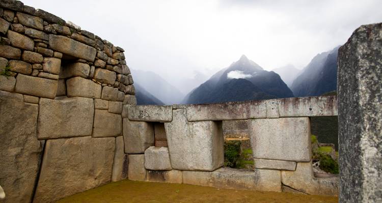 Ventanas de piedra de un edificio de Machu Picchu enmarcando los picos andinos brumosos de fondo.