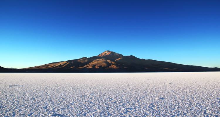 Vaste étendue blanche infinie du Salar d'Uyuni avec une montagne solitaire s'élevant sous un ciel bleu sans nuages.