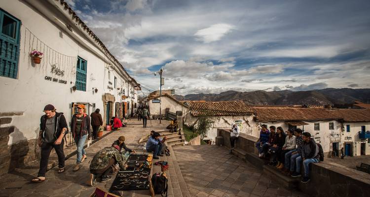 Scène animée de rue à Cusco avec des artisans vendant des objets artisanaux et des voyageurs se relaxant sur des marches en pierre.