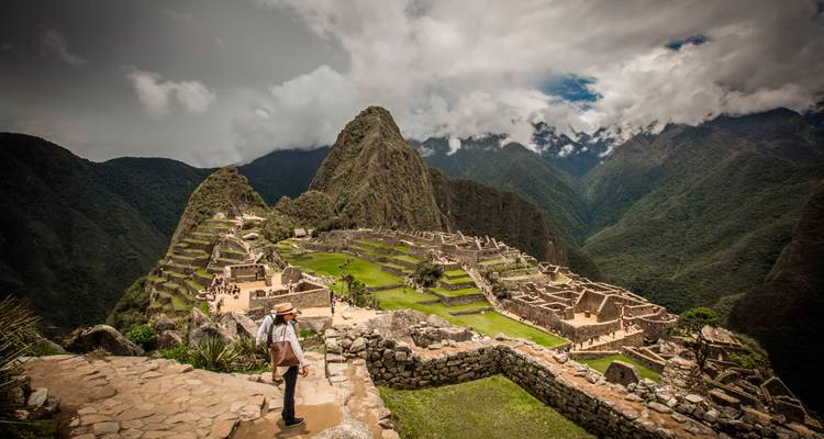 Vue panoramique des ruines du Machu Picchu entourées de pics verdoyants avec des visiteurs explorant les anciennes terrasses en pierre.