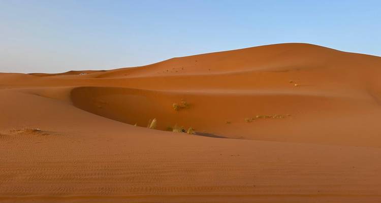 Dune de sable orange lisse sous un ciel bleu clair dans le désert marocain