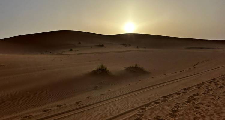 Le soleil se levant derrière une dune basse projetant de longues ombres et des empreintes de pas sur le sable