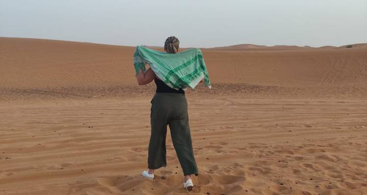 Une femme marchant sur le sable du désert tenant une écharpe verte sur ses épaules