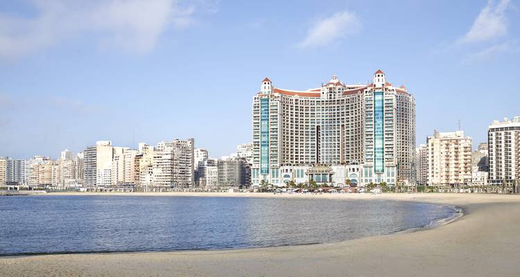Grand beachfront hotel complex and city skyline overlooking a calm Mediterranean bay.