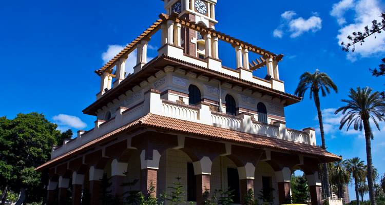 Historic clock-tower pavilion with arched windows and palm trees under a deep blue sky.