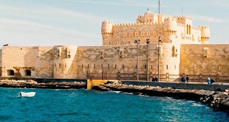 Stone Fort Qaitbay on the Mediterranean shoreline with small boat in foreground and blue waters.