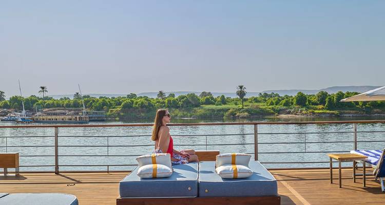 Woman resting on deck daybed overlooking calm Nile waters and verdant banks