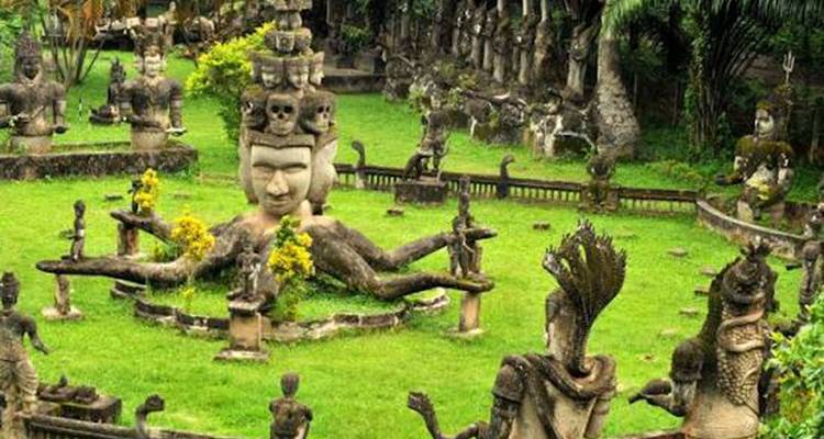 Üppiger Garten voller fantastischer Hindu-buddhistischer Steinskulpturen, darunter eine mehrköpfige Figur und eine liegende Gottheit.