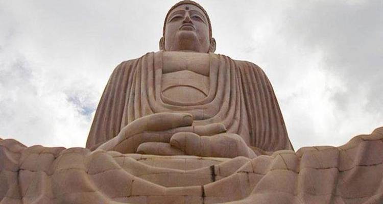Vue en contre-plongée d'une immense statue de Bouddha en pierre se détachant contre un ciel nuageux.