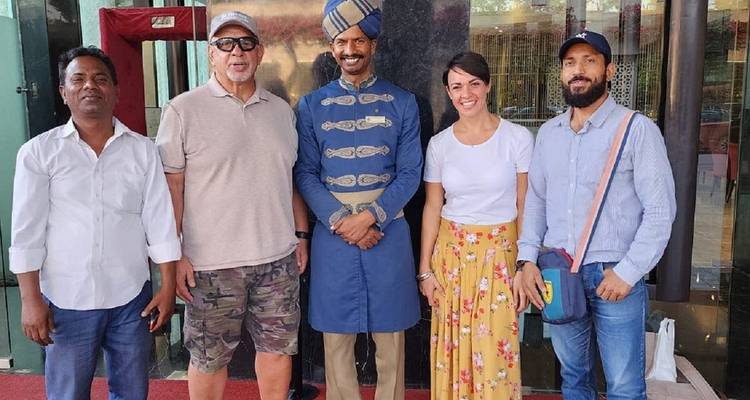 Five people, including a traditionally dressed hotel doorman, pose for a group photo outside a building entrance.