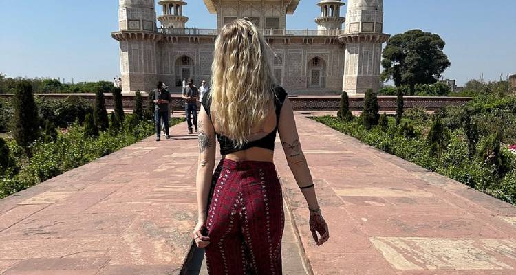 Una mujer con pantalones coloridos camina por un sendero de piedra hacia una tumba blanca mogol en un día soleado.