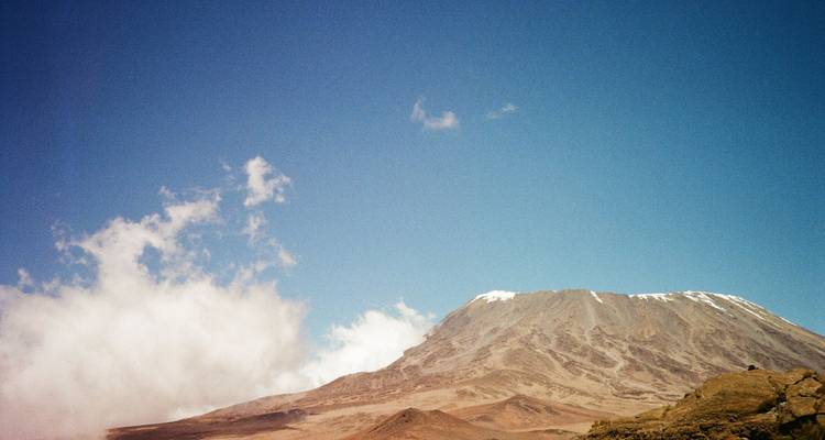 Portrait latéral du pic du Kilimandjaro avec des nuages qui dérivent sur un ciel éclatant.
