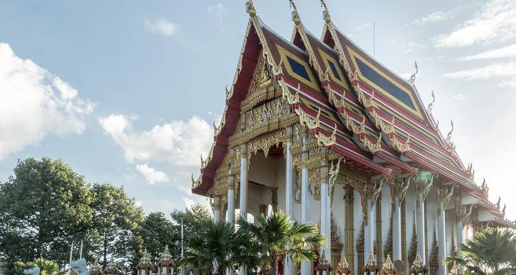 Een sierlijk Thai tempel met vergulde trapsgewijze daken en witte zuilen gloeit in zacht daglicht.