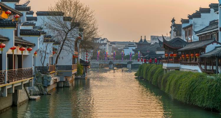 Traditional white-walled houses with red lanterns line a tranquil canal at dusk.
