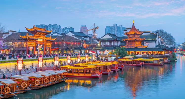 Colorful illuminated pavilions and boats reflect on a riverfront during blue hour.