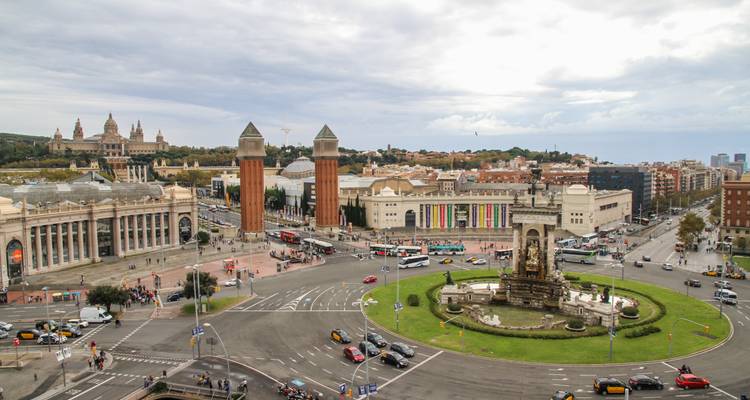 Elevated panorama of Plaça d’Espanya in Barcelona with Venetian Towers, National Palace and traffic circling a fountain.