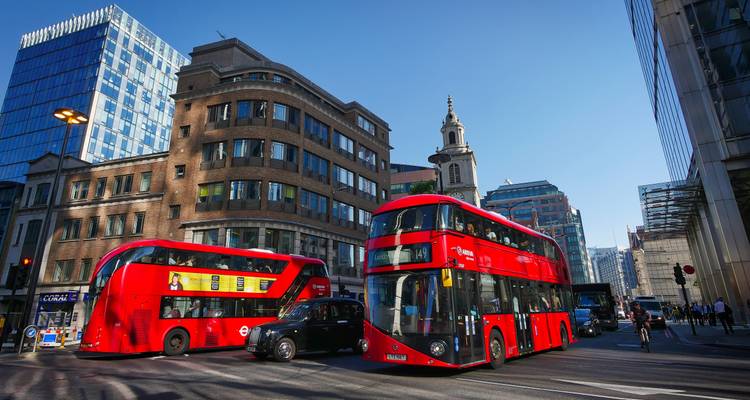 Busy London intersection with two iconic red double-decker buses, a black cab and modern office blocks.