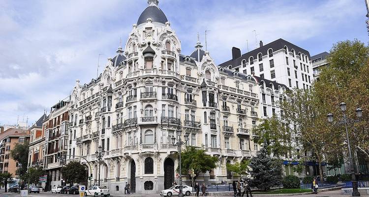 Elegant white Belle Époque building on a Madrid street corner under a partly cloudy sky.