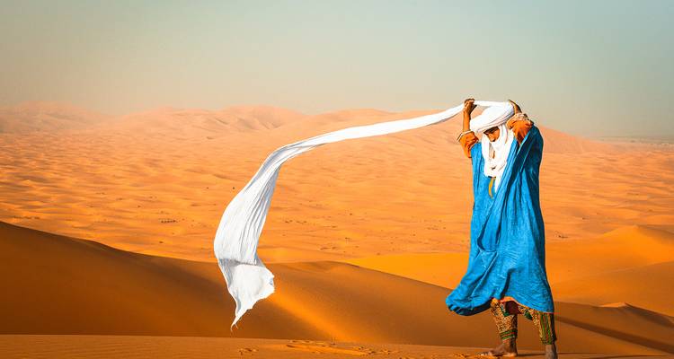 Un homme berbère vêtu d'une robe bleu vif laisse un long foulard blanc flotter dans la brise du désert.