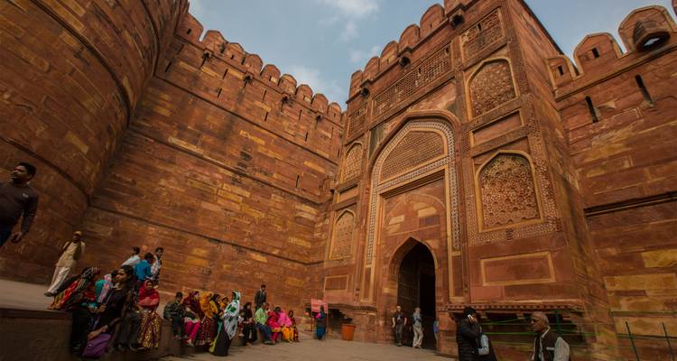Los visitantes descansan bajo los imponentes muros de arenisca roja y las puertas ornamentadas del Fuerte de Agra.