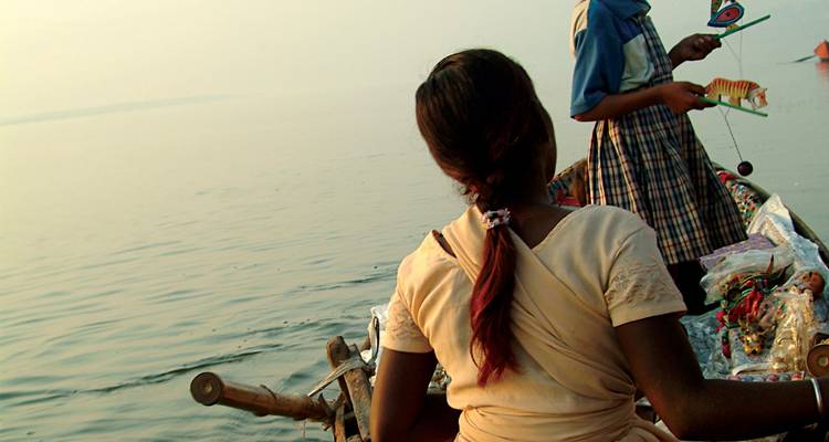 Las mujeres venden baratijas desde una barca de madera en el río Ganges tranquilo y brumoso.