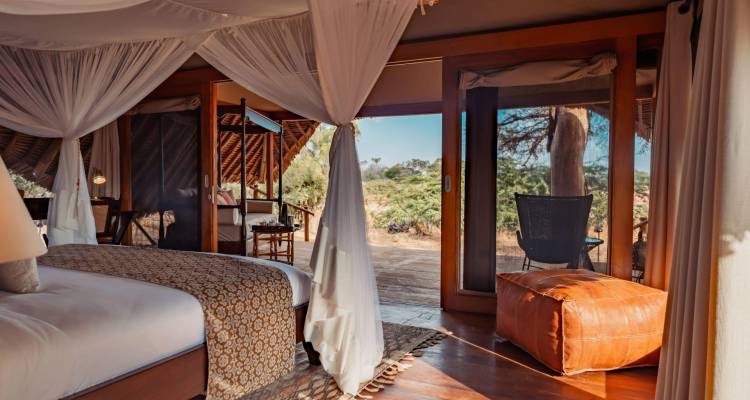 Luxurious safari tent bedroom opening onto a wooden deck overlooking bushland and clear skies