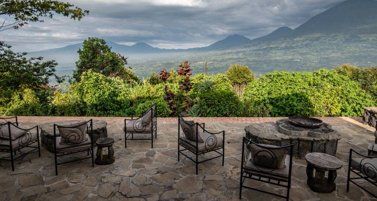 Stone terrace with wrought-iron chairs overlooking lush forest and volcanic peaks under dramatic skies