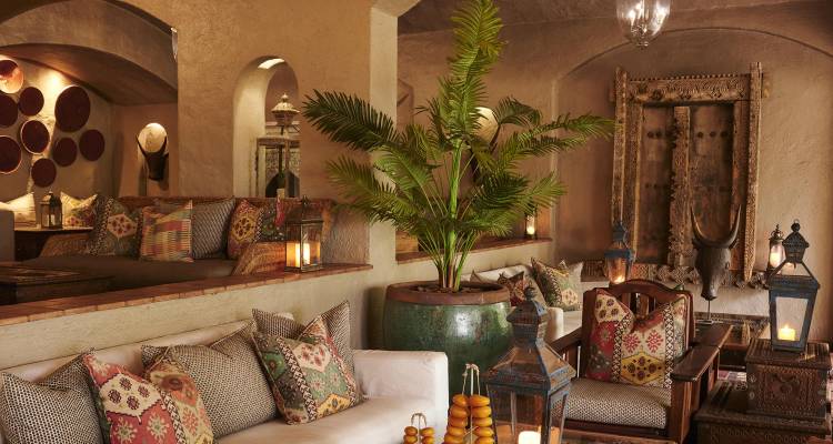 Elegante sala de lodge con cojines estampados, linternas y exuberantes palmeras en macetas