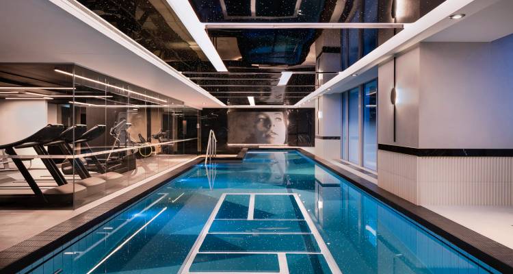 Sleek indoor lap pool with mirrored ceiling, treadmills and contemporary lighting in a luxury hotel.