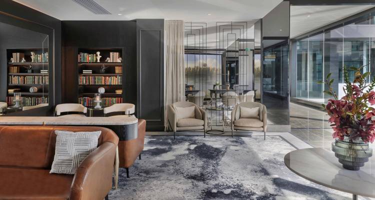 Chic hotel lounge featuring leather sofa, art-deco shelving and marble accents with floor-to-ceiling windows.
