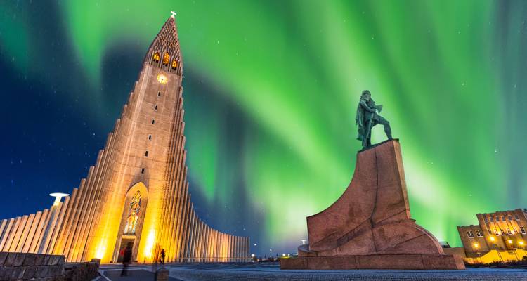 Northern Lights dancing above Hallgrímskirkja church and Leif Erikson statue in Reykjavik at night.