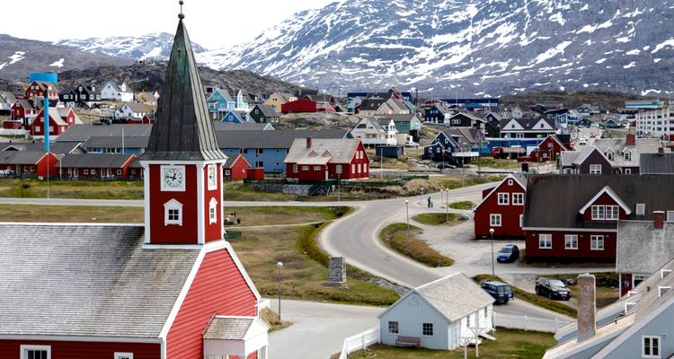 Colourful wooden buildings and red church spire of Nuuk with snowy hills in the background.
