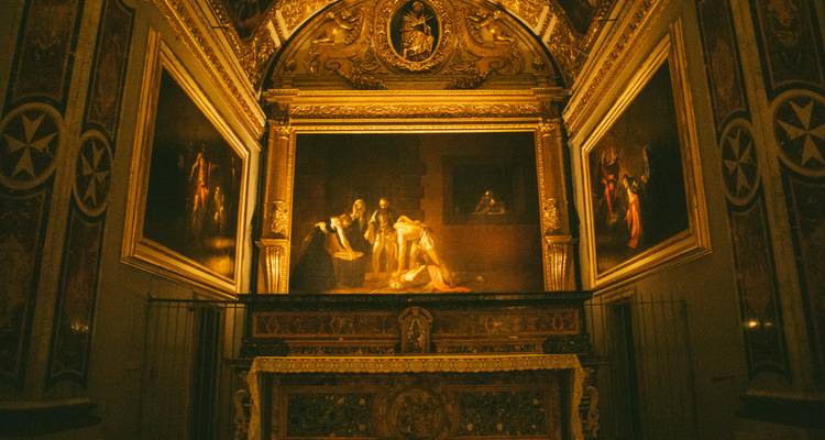 Dimly lit chapel altar featuring a dramatic Caravaggio-style painting and ornate wooden frame