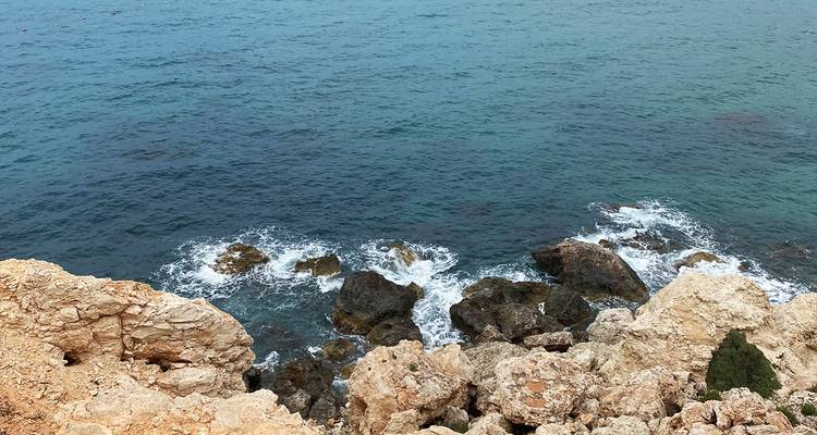 Rough limestone rocks with small waves breaking over dark boulders below