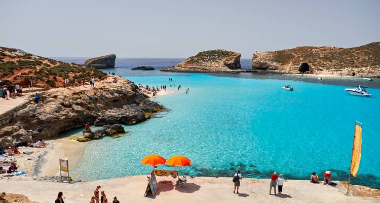 Iconic bright-blue lagoon with bathers wading in crystal water, rocky islets and cave backdrop