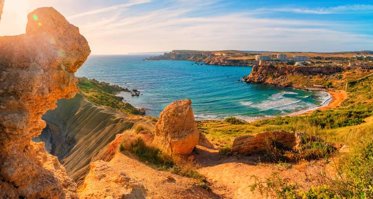 Warm sunset light over rugged coastal cliffs and sweeping bay with sparkling sea