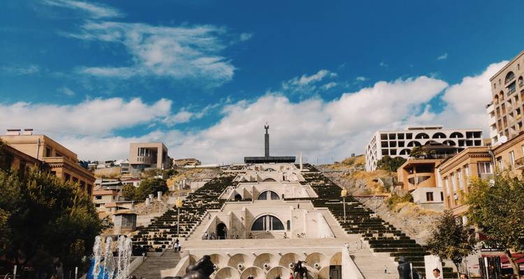 The monumental limestone stairway of Yerevan Cascade ascending toward an obelisk beneath a bright blue sky.
