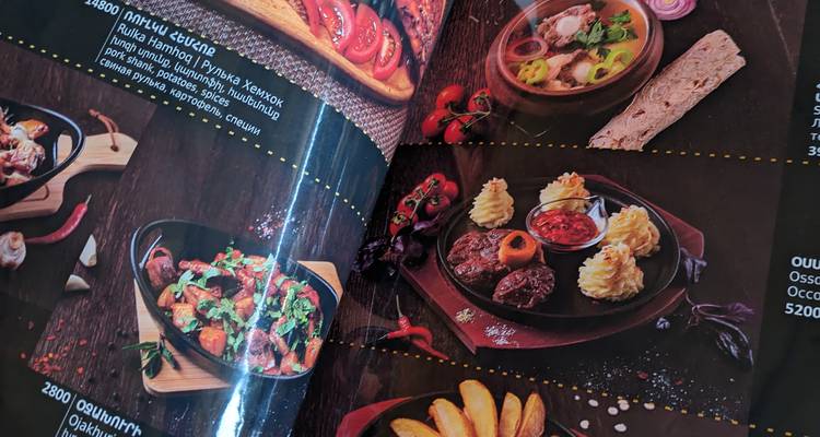 Glossy restaurant menu showing plated Armenian dishes and prices under reflective lighting.