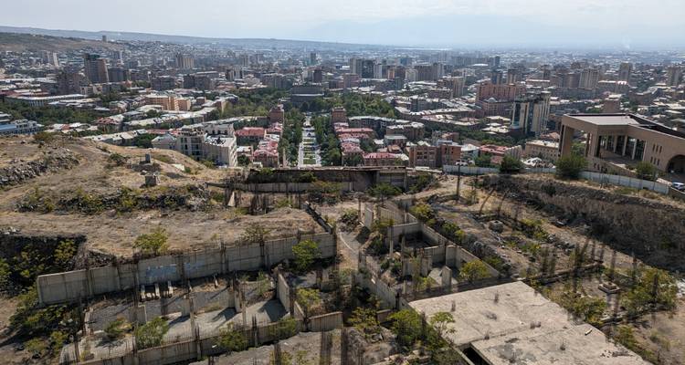 High aerial view over Yerevan city with green Cascade gardens leading toward distant suburbs and hazy hills.
