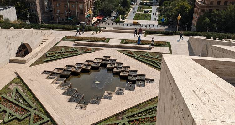 Geometric fountain pools and landscaped designs atop the Yerevan Cascade with visitors walking around.