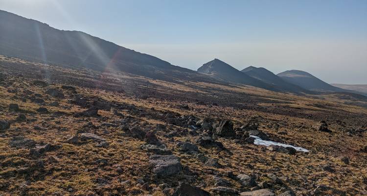 Sunlit mountain ridges casting long shadows over a rocky high-altitude plateau.