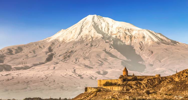 Iconic Khor Virap monastery perched on a rocky hill with majestic snow-capped Mount Ararat towering behind.